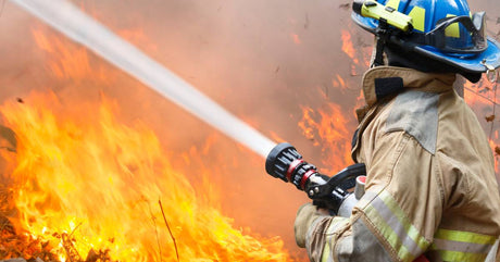 A wildland firefighter, from behind, is operating a hose with a nozzle that is blasting out a stream of water.